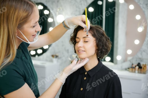 Preview: Makeup artist doing eyebrow correction for woman in beauty salon.