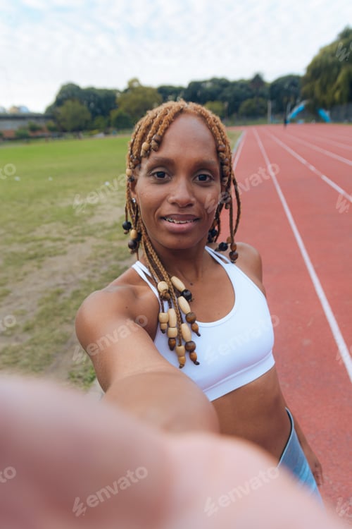 Preview: Sporty African woman on running track taking vertical selfie portrait with mobile phone