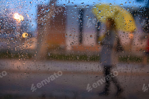 Preview: Woman holding a yellow umbrella shot through raindrops on a windo
