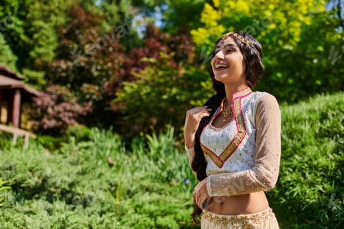 Preview: excited indian woman in traditional attire laughing near greenery in summer park