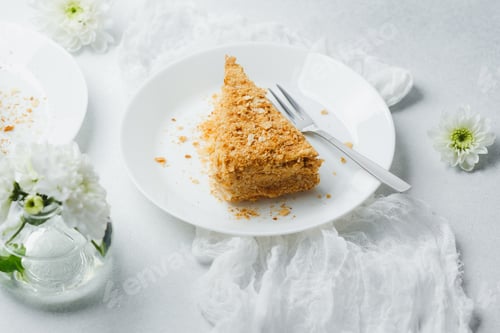 Preview: Napoleon cake dessert with pastry cream and puff layers on white plate with fork and flowers