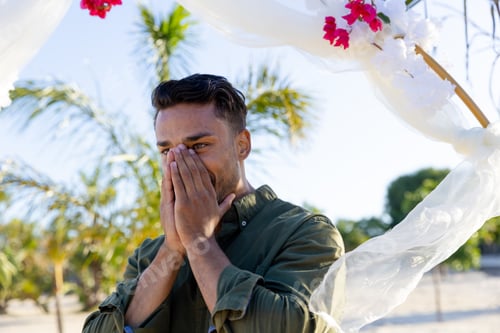 Preview: Nervous caucasian groom with covering face with hands against decoration at wedding ceremony