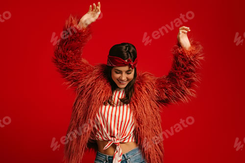 Preview: Stylish young hipster woman wearing fluffy coat and dancing on red background
