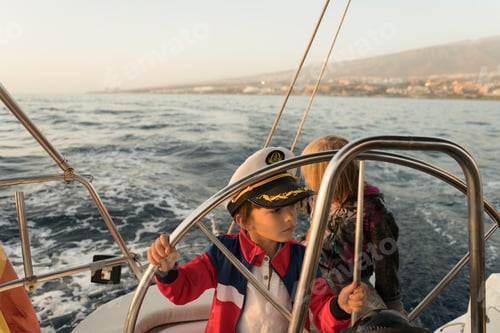 Preview: Smiling children holding steering wheel on yacht on water