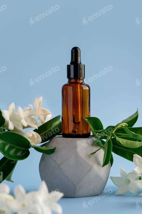 Preview: Amber glass serum dropper with fresh flowers around on cement podium,blue background