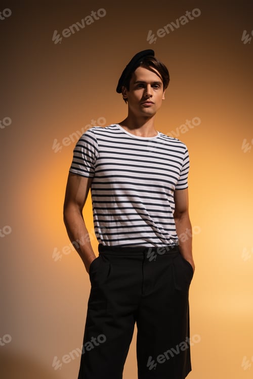 Preview: man in beret and striped t-shirt standing with hands in pockets on orange