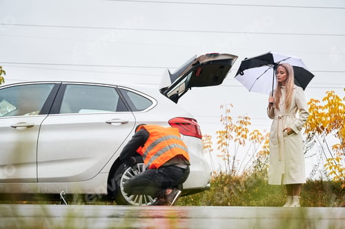 Preview: Emergency mechanic repairing young woman vehicle on the street.