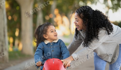 Preview: Hispanic mother having fun with her son riding toy motorcycle in park