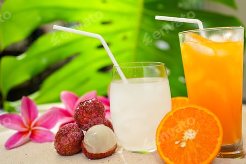 Preview: Closeup shot of a glass of orange juice, a cocktail, next to lychees and plumerias