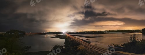 Preview: A panoramic night view showing a luminous cityscape beyond a calm river