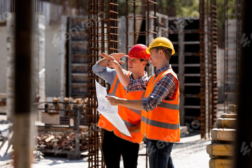 Preview: Structural engineer and construction manager in orange work vests and hard helmets explore