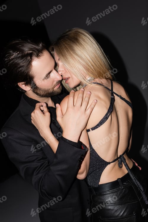 Preview: Bearded man kissing sexy blonde girlfriend on grey background