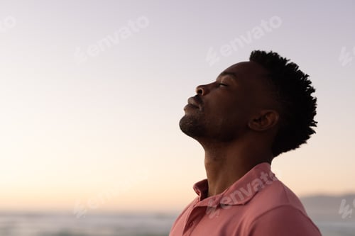 Preview: Side view of african american young man with eyes closed at beach against clear sky during sunset