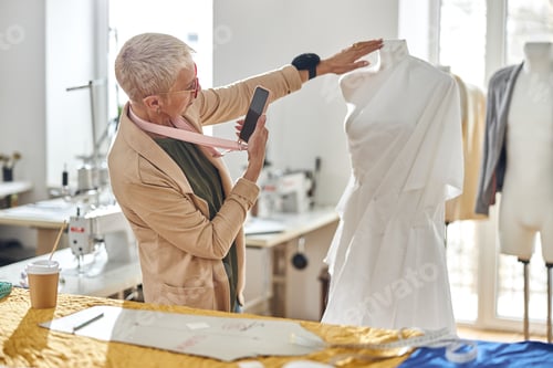 Preview: Professional dressmaker takes picture of mannequin wrapped with white fabric in workshop