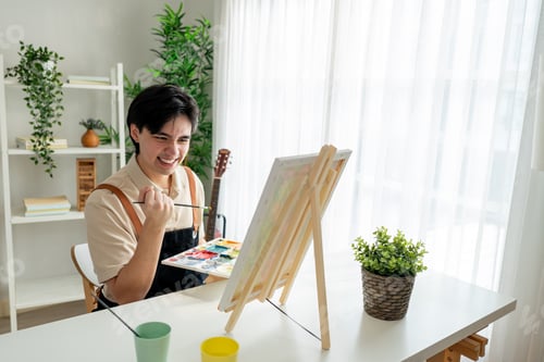 Preview: Asian young talented man artist coloring on painting board in house.