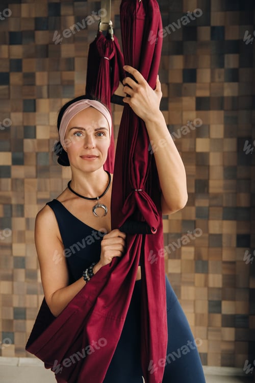 Preview: A woman does yoga on a burgundy hanging hammock in the gym