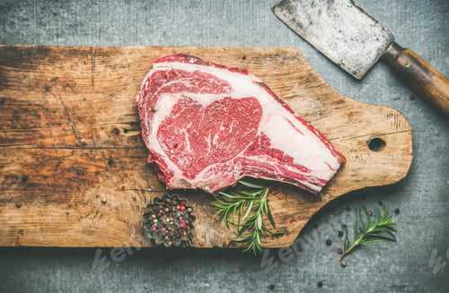 Preview: Raw beef steak rib-eye on board with seasoning and knife