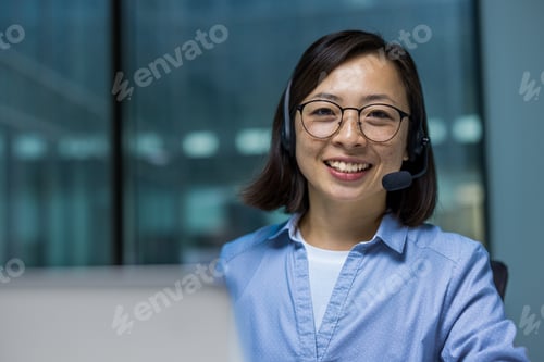 Preview: Asian businesswoman wearing headset and glasses smiling in a modern office