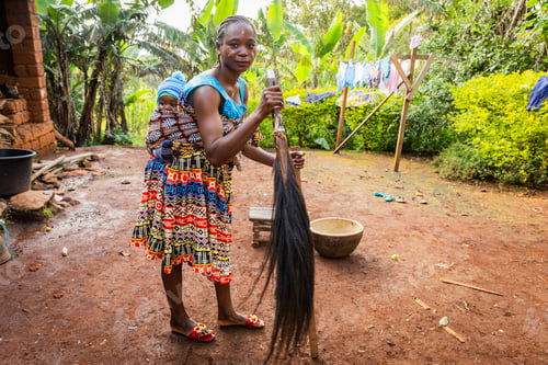 Preview: Young African mother with her baby tied to her back in a loincloth holding a ponytail in her hands