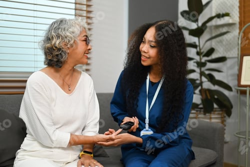 Preview: Smiling African nurse checking blood glucose levels of senior diabetic woman during a home visit.
