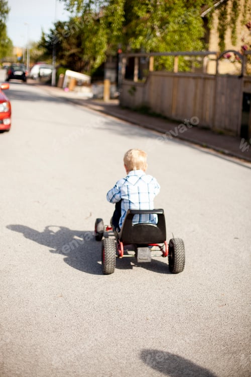 Preview: Rear view of boy riding quadricycle on street