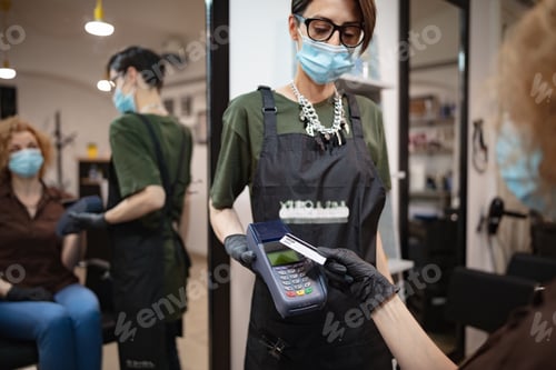 Preview: Paying With Contactless Card. Hairdresser And Customer In A Salon With Medical Masks During Virus