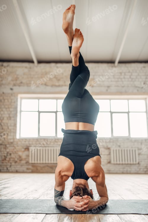 Preview: Male yoga stands on the head in gym