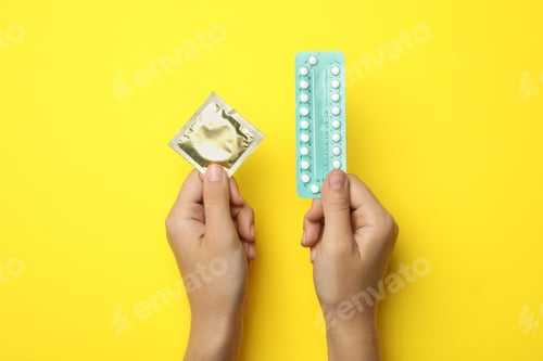 Preview: Woman holding condom and birth control pills on yellow background, top view. Safe sex