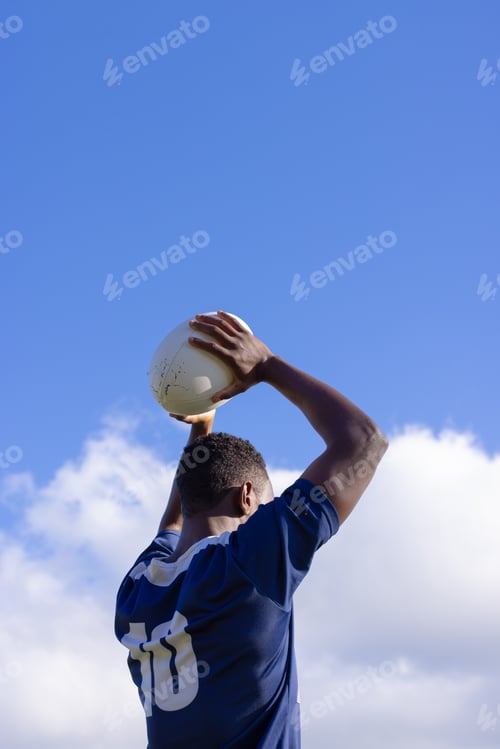 Preview: African American young male athlete holding a rugby ball, ready to throw, copy space