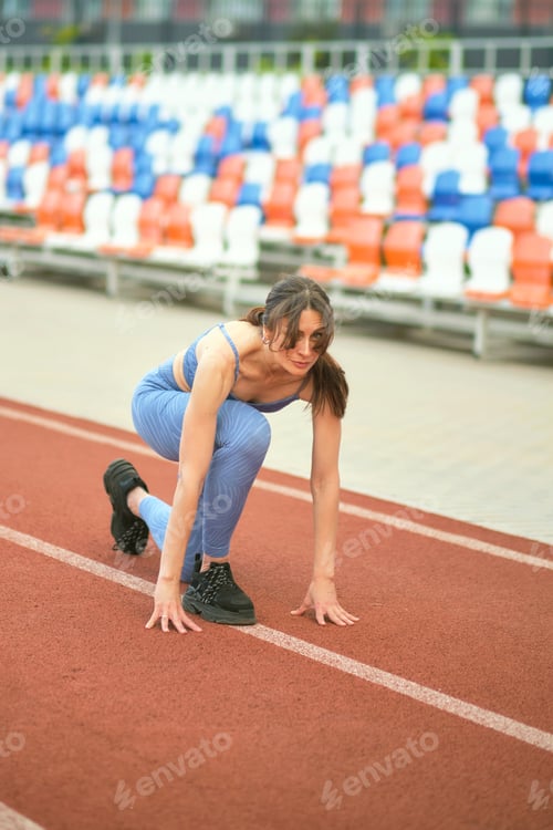 Preview: woman, dressed in blue athletic gear, assumes a starting stance on a track, showcasing her readiness