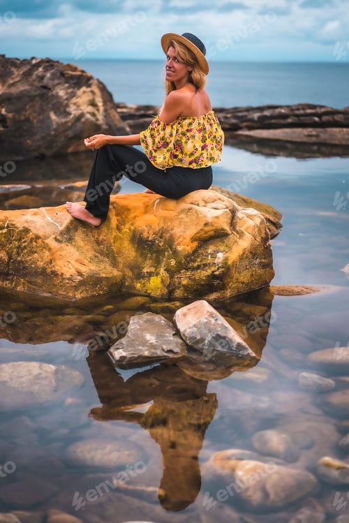 Preview: Girl in a floral shirt, black shorts and straw hat in a natural landscape by the sea