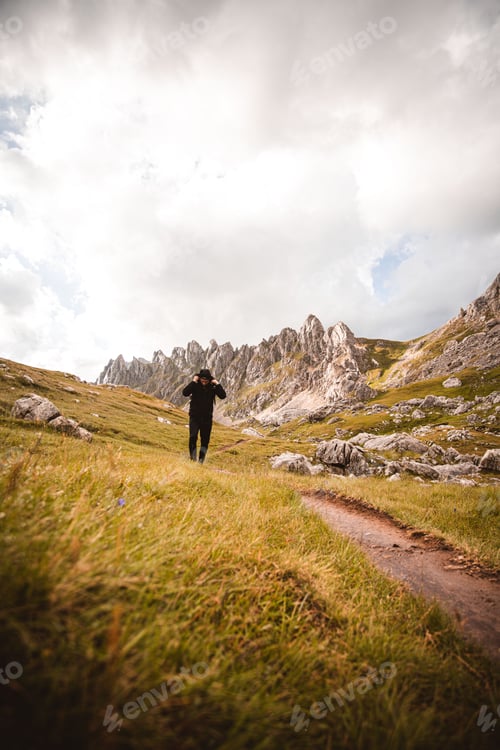 Preview: Young man wearing a black jacket striding through a lush green landscape