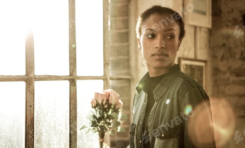 Preview: Young woman standing indoors by a window, looking away.