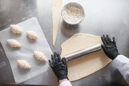 Preview: Baker rolling dough with rolling pin, making croissants in bakery