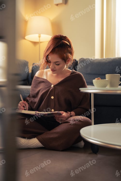 Preview: A calm woman writes in her journal at home while sitting on the floor,