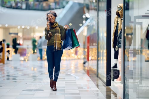 Preview: Happy black woman talking on cell phone while shopping at the mall.