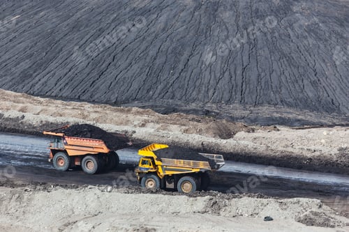 Preview: Two large yellow dump trucks transport loads of coal in an open-pit mining site.