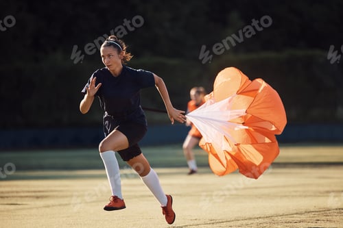 Preview: Young athletic woman with parachute running during soccer training on playing field.