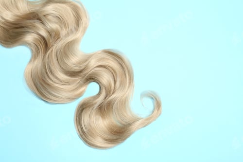 Vista previa: Lock of blonde wavy hair on color background, top view. Space for text