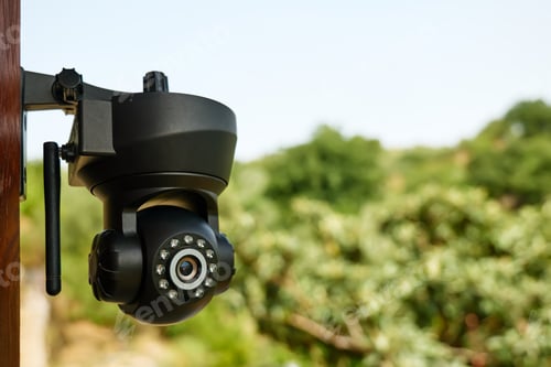 Preview: Security camera on the wall of a building with nature in background.