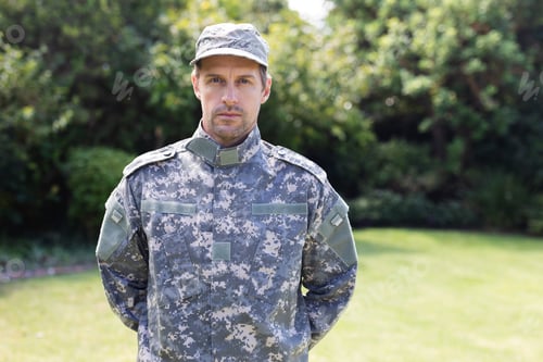 Preview: Portrait of caucasian male soldier wearing camo fatigues and cap standing in garden