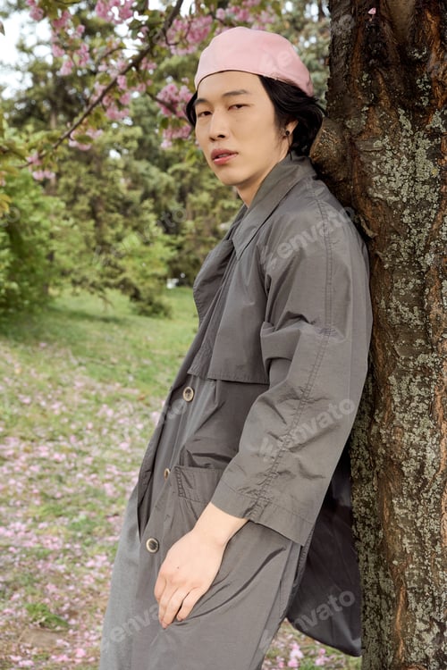 Preview: Stylish young man in grey trench coat enjoys a serene day at the park