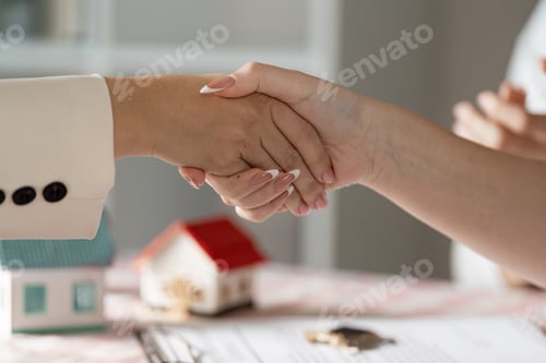 Preview: Real Estate Agent Shaking Hands with Client Over Contract and Model House on Table