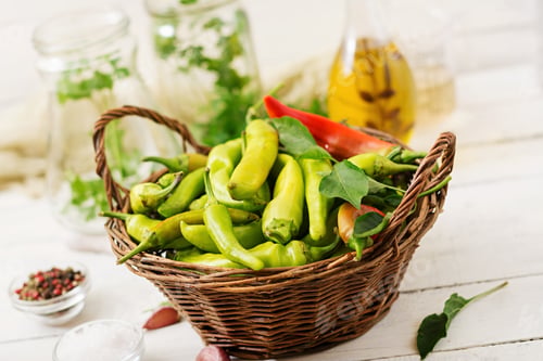Preview: Green chili peppers in a basket on a white background. Preparation for pickling.