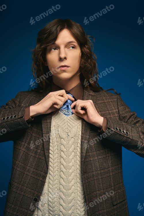 Preview: Handsome young man adjusting his stylish tie against a vibrant blue backdrop