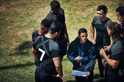 Preview: Cropped shot of a handsome young rugby coach addressing his team on the field during the day