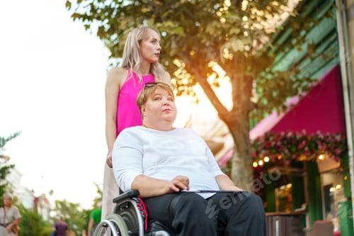 Preview: Young woman helping mature woman in wheelchair in the city