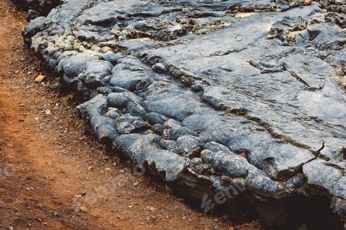 Preview: Cooled lava touching the dirt where it stopped running, forming a curved edge of black volcanic rock