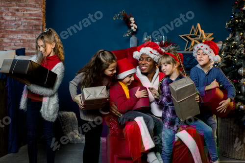Preview: African Santa Claus sits on a background of a Christmas tree and presents gifts to the children