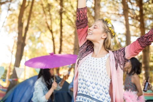Preview: Happy woman with eyes closed raising hands at campsite